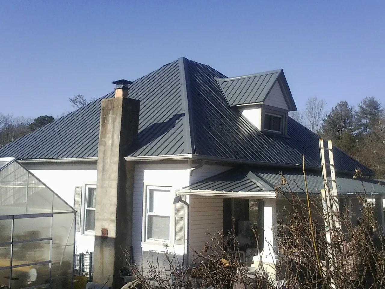 Dark blue standing seam metal roof on a white farmhouse with dormer — Slate & Tile Roof Repair by Roofing Brothers in Wetmore