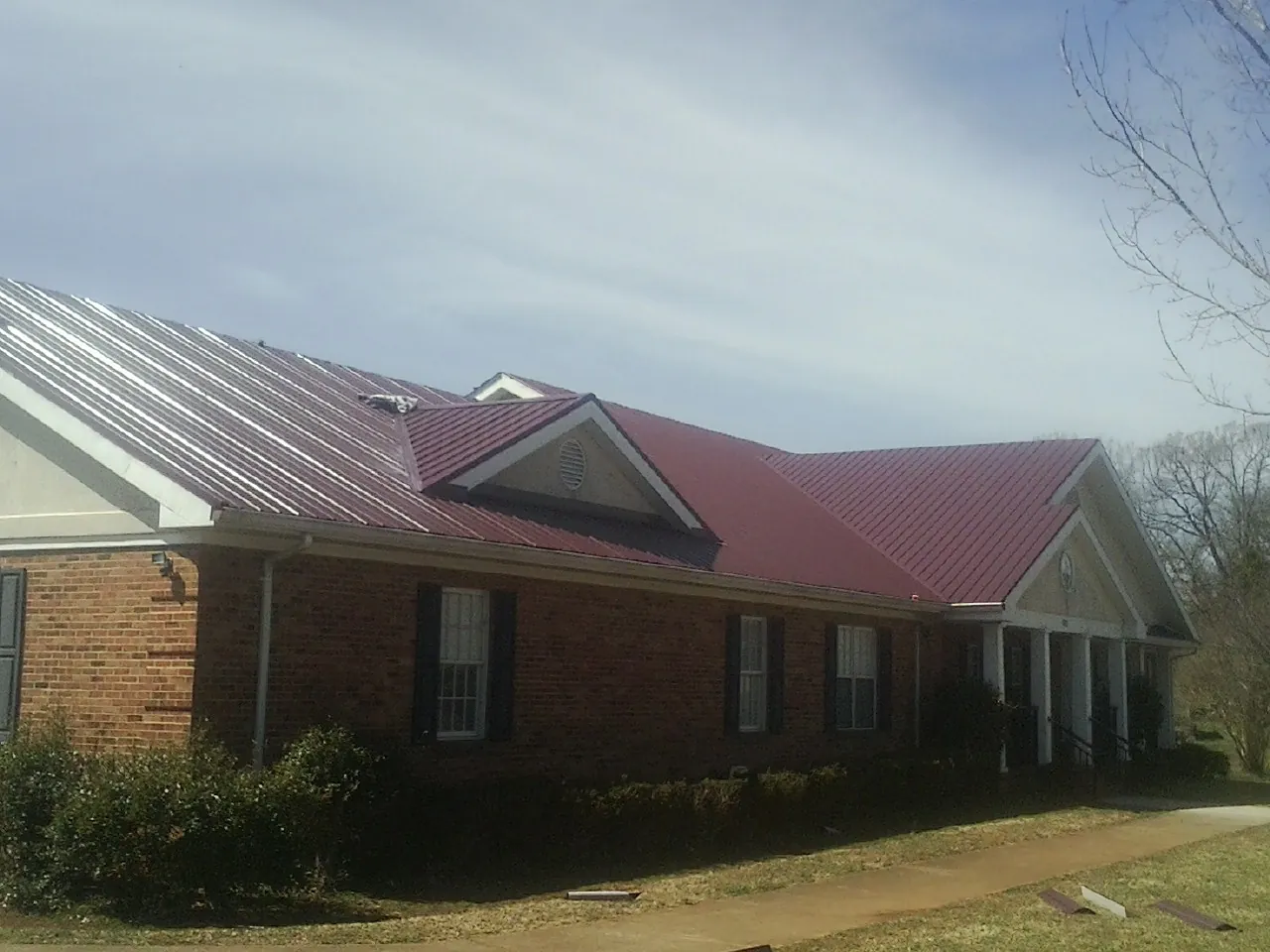 Red metal roof with gabled entries on a long brick building, from a Hail Damage Roof Repair job in Wetmore