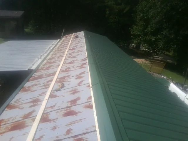 Old rusted panels beside newly installed green metal roofing — Wind Damage Roof Repair by Roofing Brothers in Wetmore
