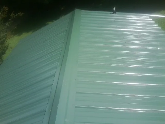 New green metal panels meeting at the ridge of a roof — Flat Roof Repair work by our crew in Wetmore