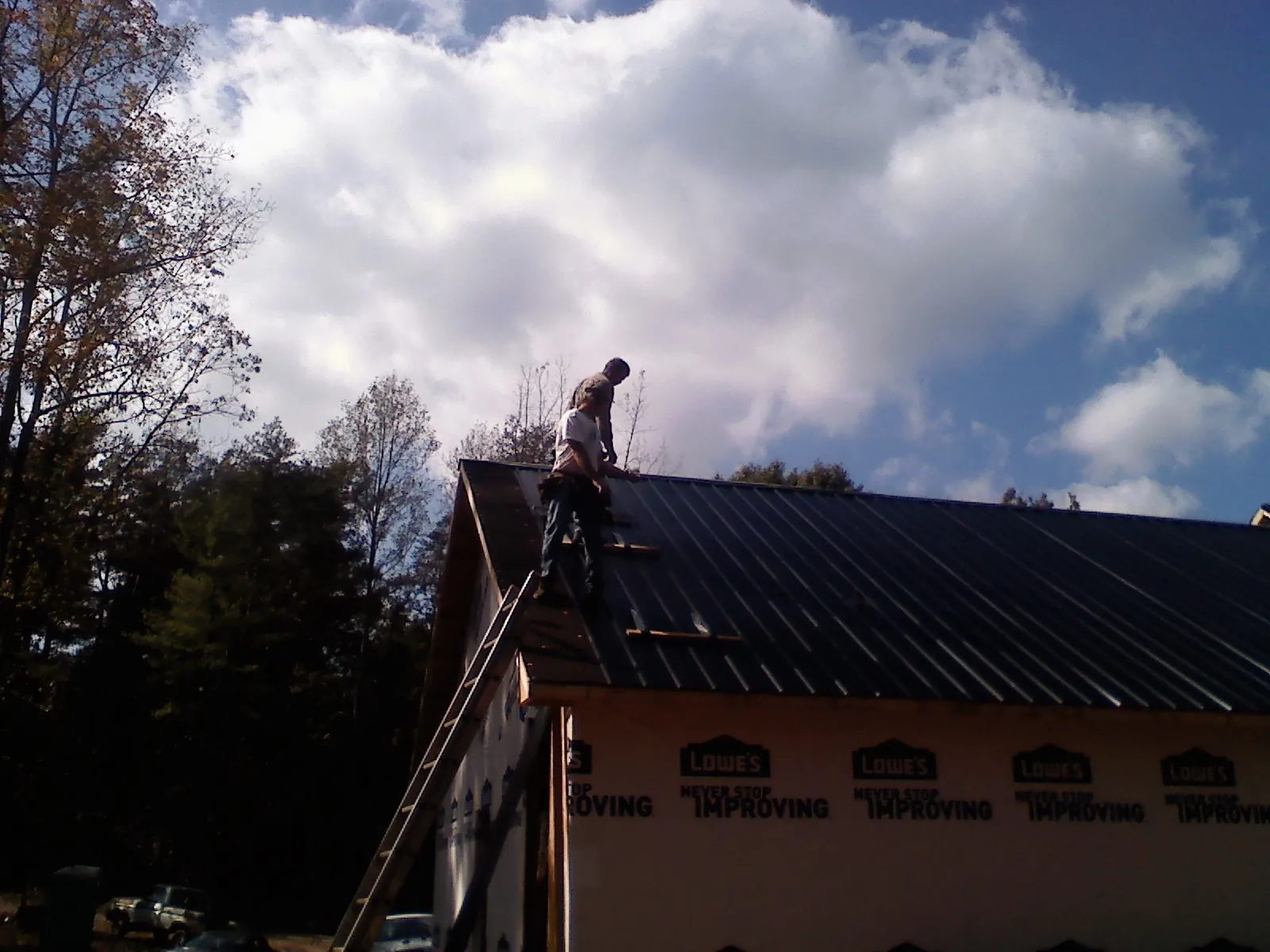 Roofer fastening dark metal panels high against a cloudy sky, from a Roof Inspection job in Wetmore
