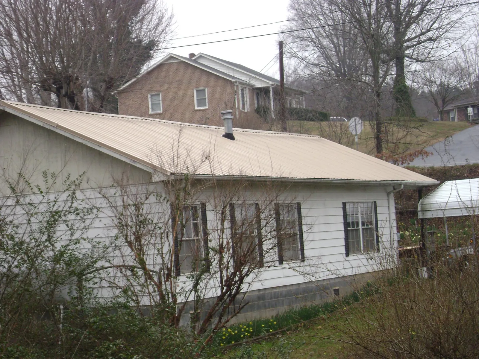 Tan metal roof on a white sided house set into a hillside — Commercial Roofing by Roofing Brothers in Wetmore